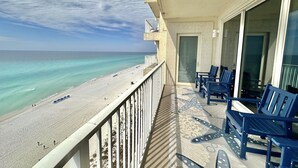A balcony with a view of the beach and ocean. There are blue chairs and a table on the balcony.