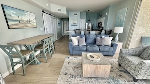 A spacious living room with a blue sofa, wooden coffee table, and a dining area with a wooden table and chairs.