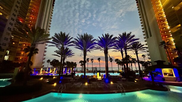 A pool area with palm trees and a view of the ocean, surrounded by tall buildings.