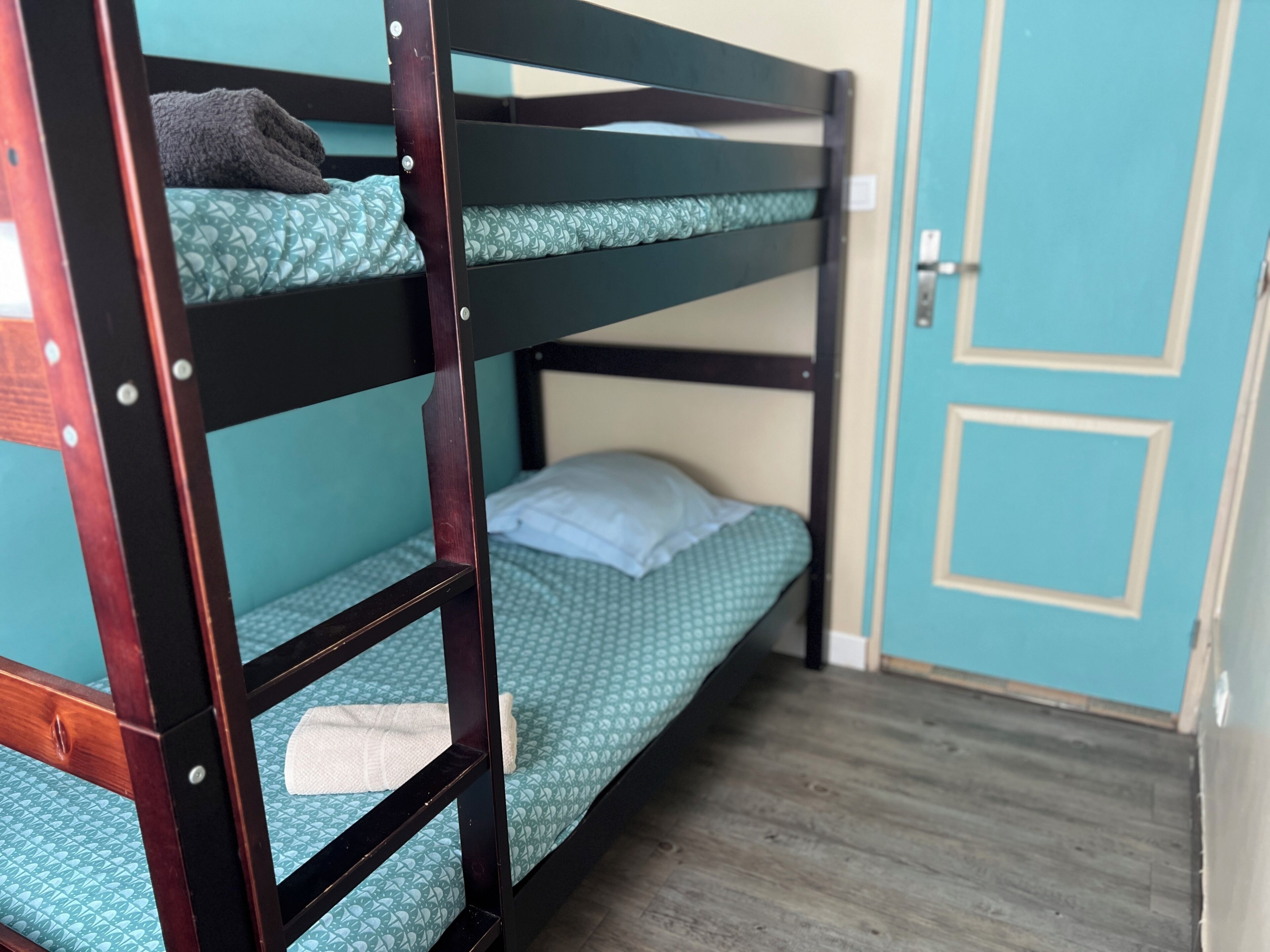 A bunk bed with a teal patterned mattress, a white pillow, and a rolled towel on the lower bunk.