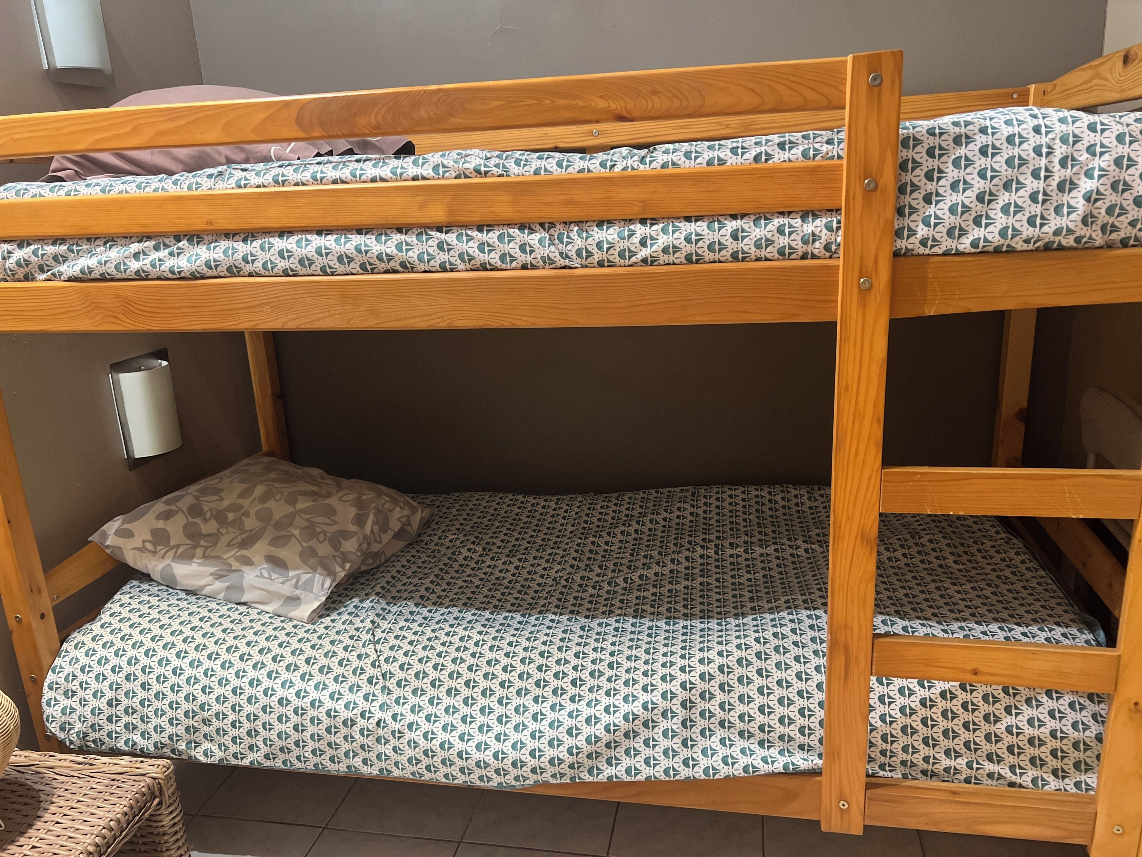 A bunk bed with patterned bedding, a wall-mounted light, and a woven basket.