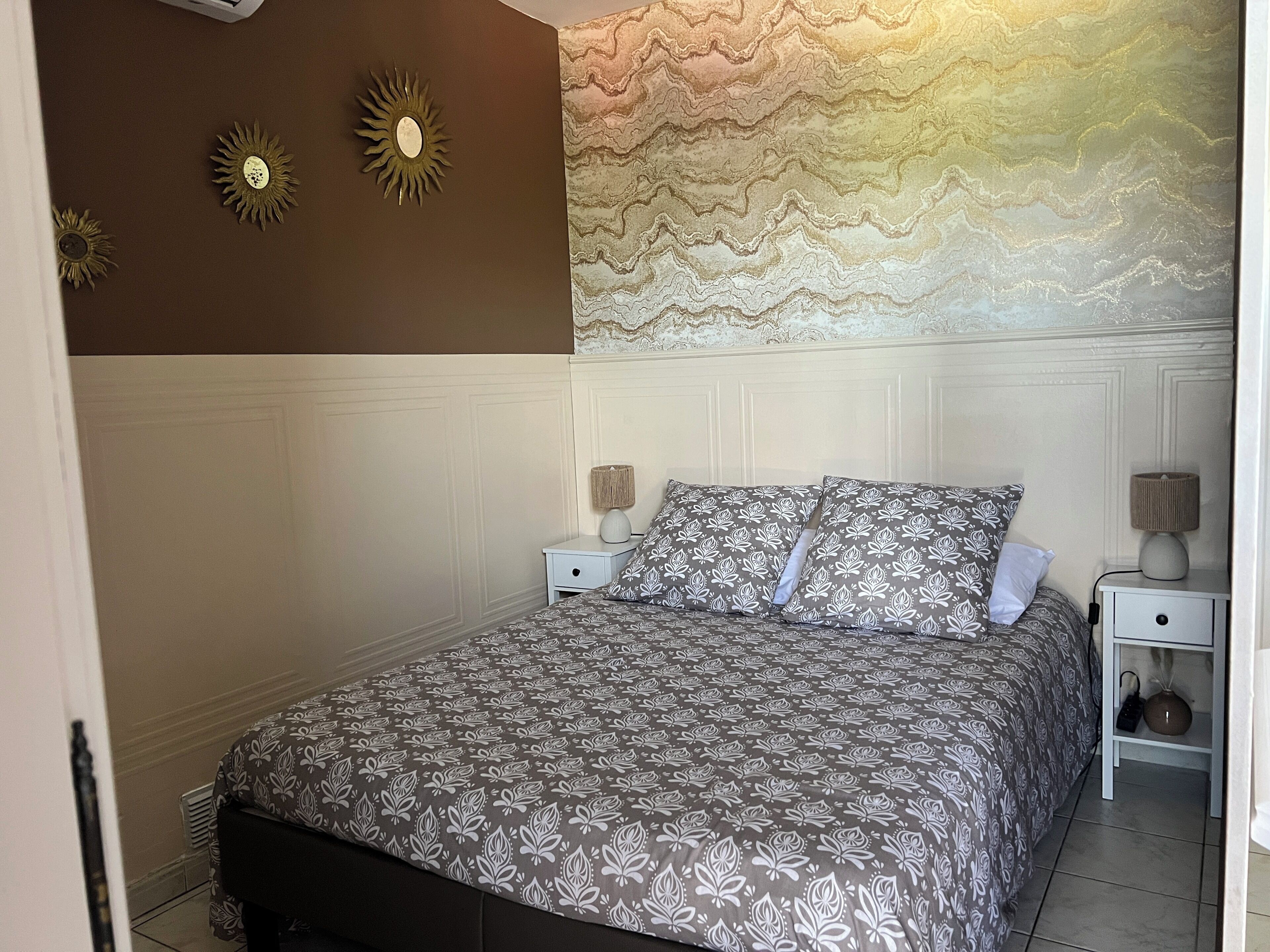 A bedroom with a bed, two bedside tables, a wall clock, and a decorative wall panel.