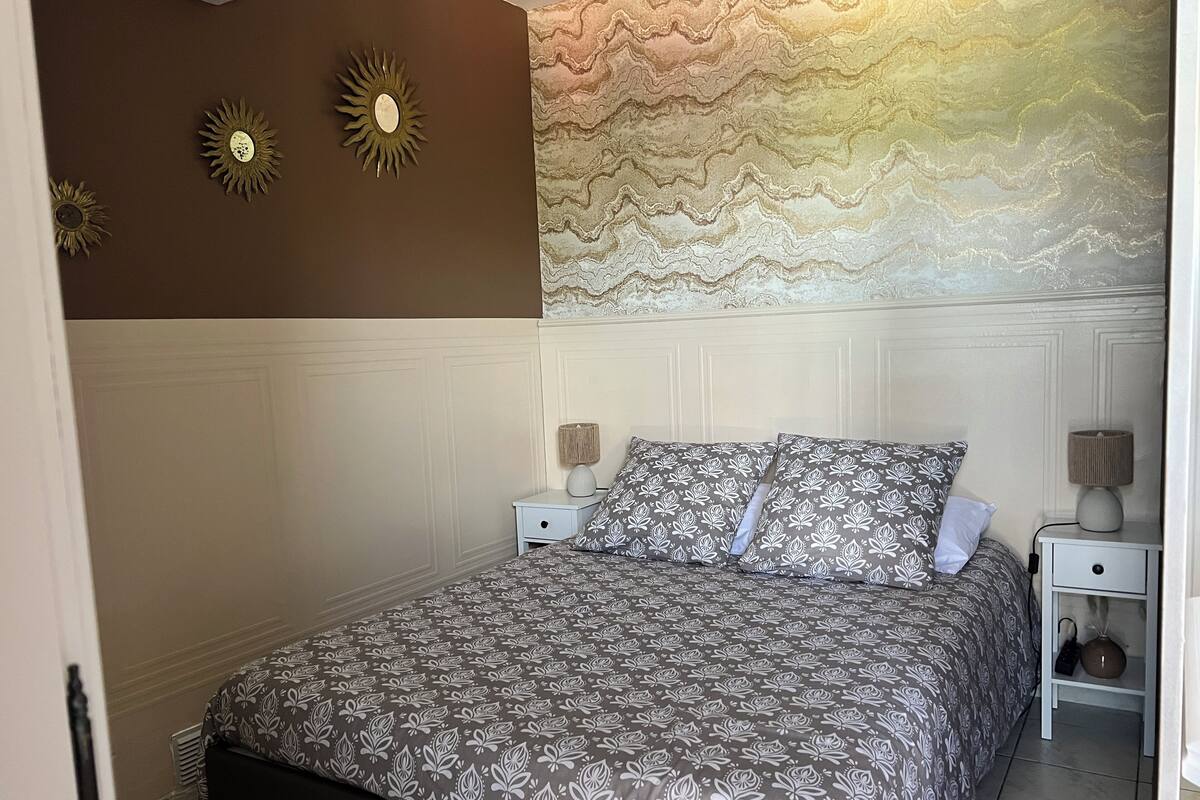 Un dormitorio con una cama, dos mesitas de noche, un reloj de pared y un panel decorativo.