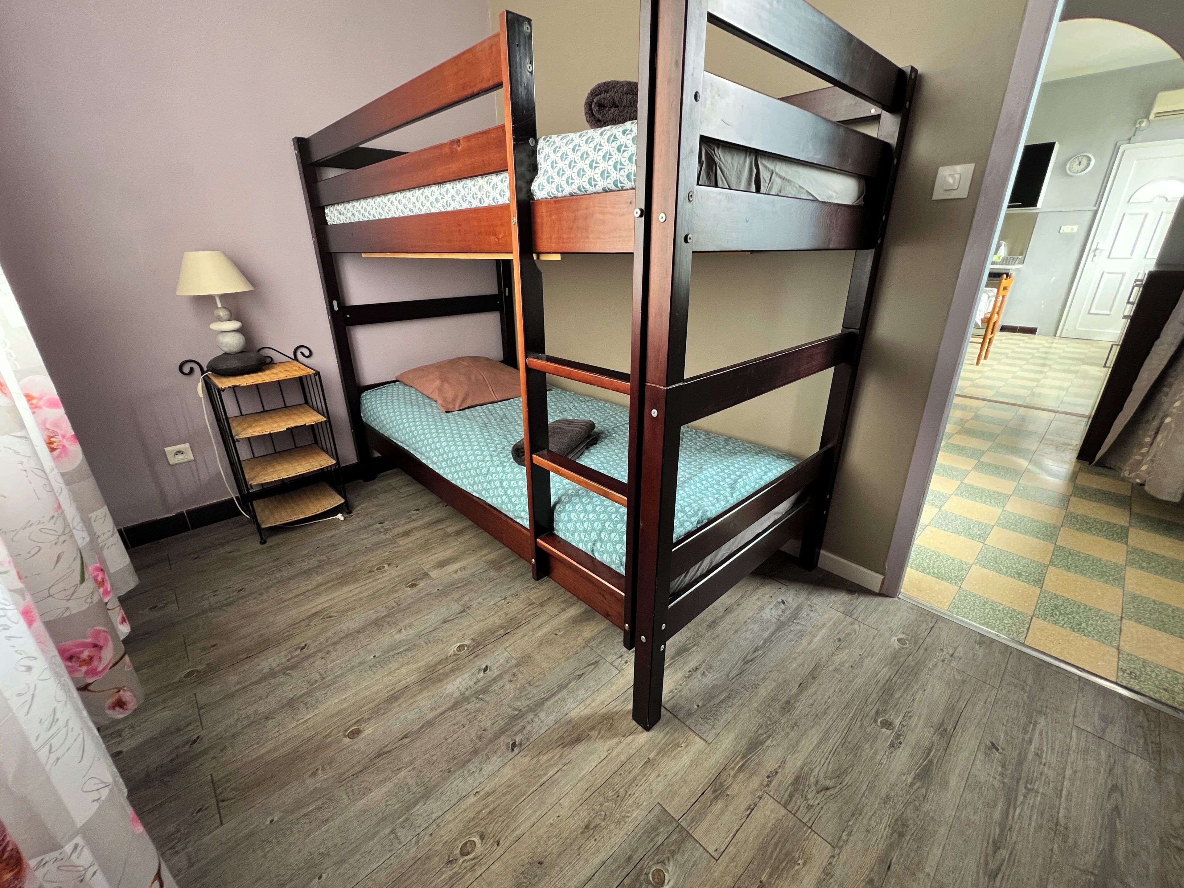 A bunk bed with a shelf, a small table with a lamp, and a patterned curtain.