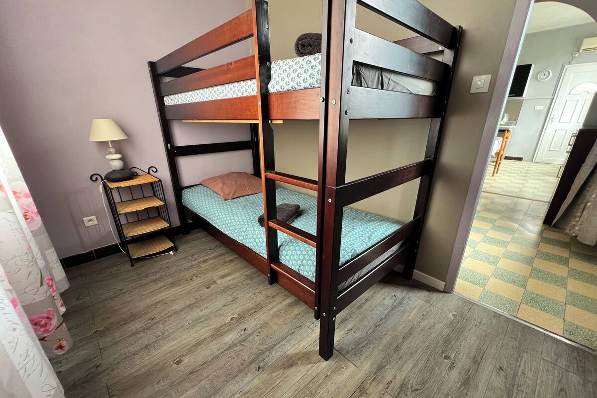 Una cama litera con un estante, una mesita con una lámpara y una cortina estampada.