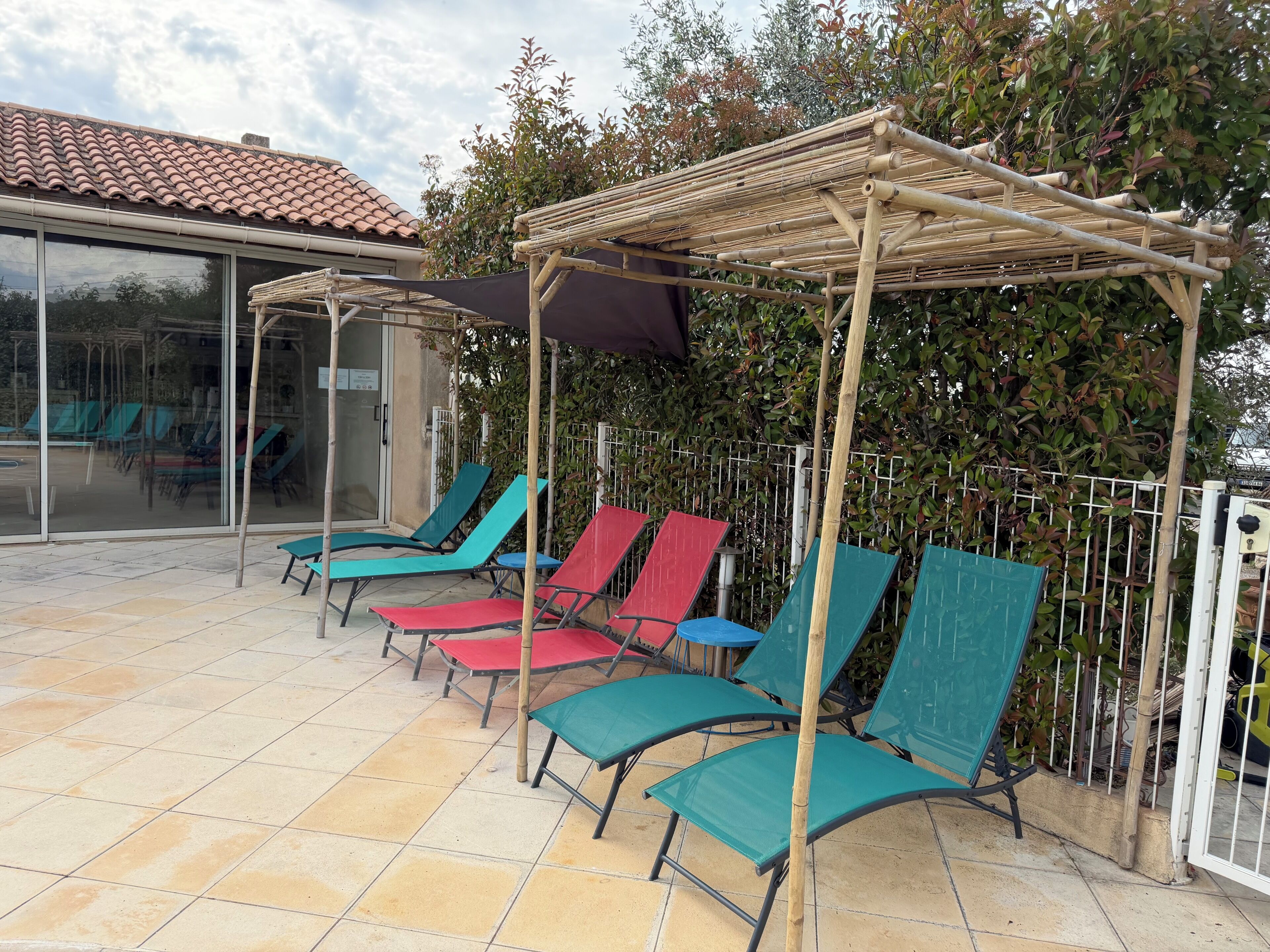 Un espacio de estar al aire libre techado con sillones reclinables, una pérgola y un ventanal de vidrio que da a una piscina.