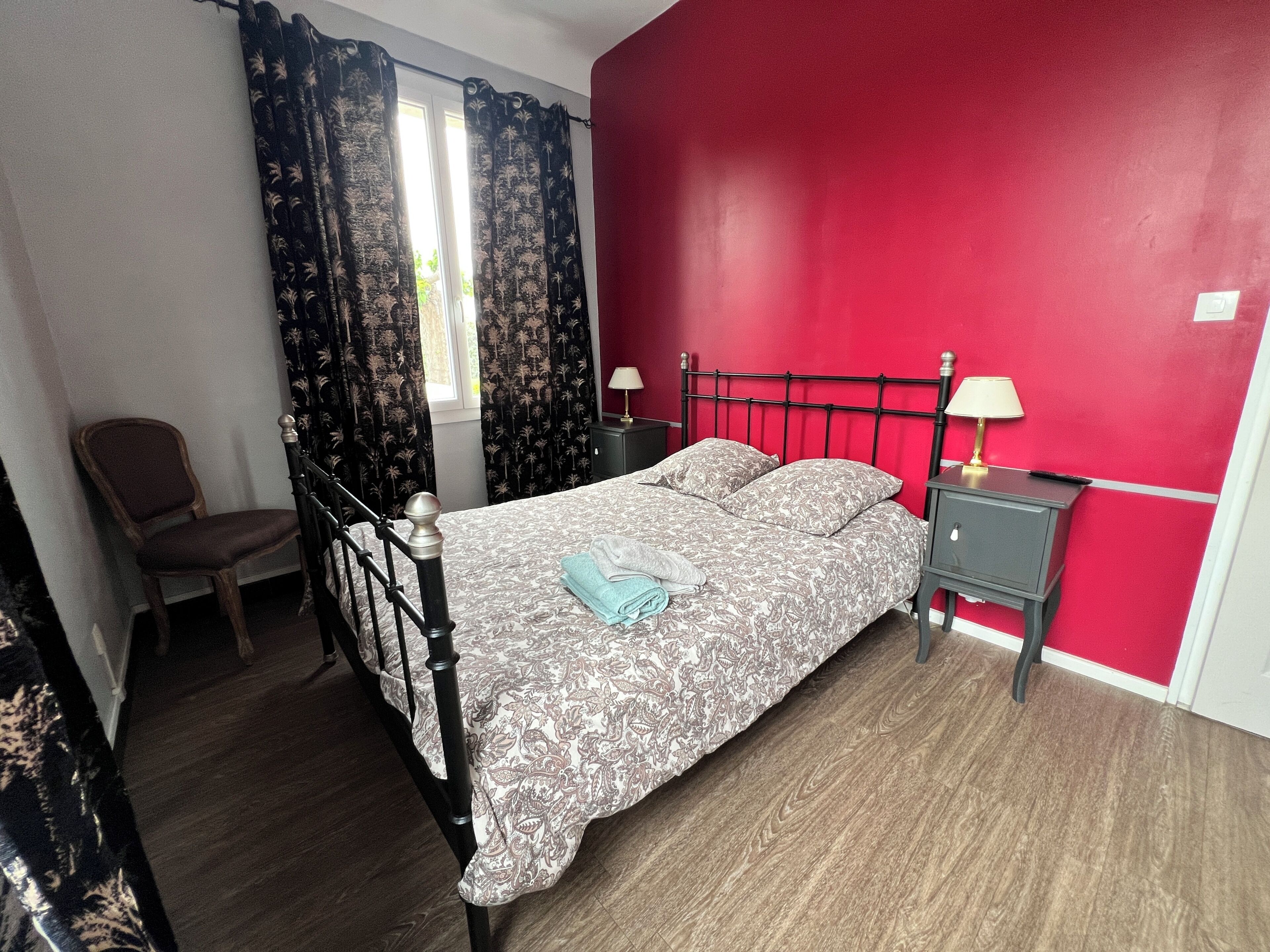 A bedroom with a bed, a chair, a nightstand, and a window with curtains.