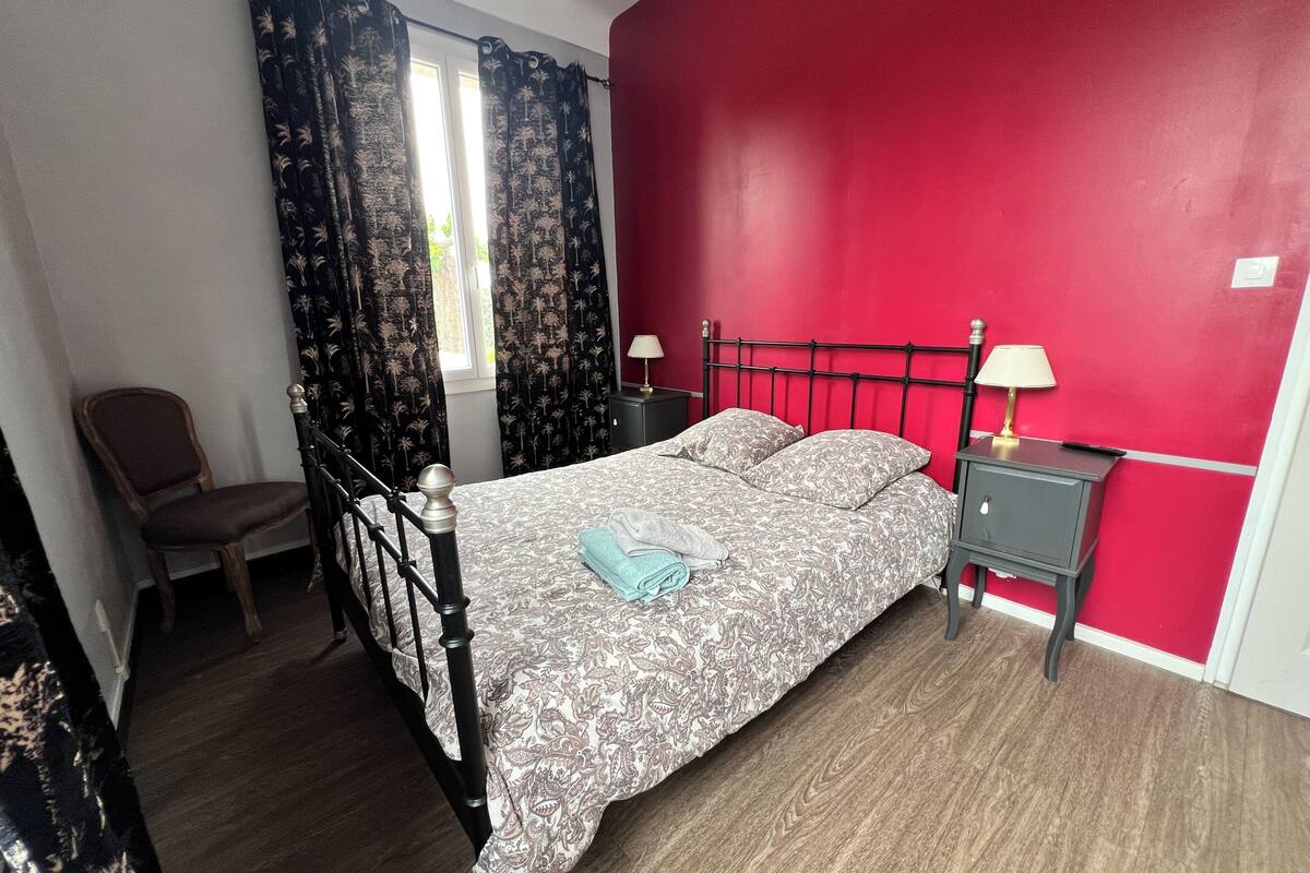 Un dormitorio con una cama, una silla, una mesita de noche y una ventana con cortinas.