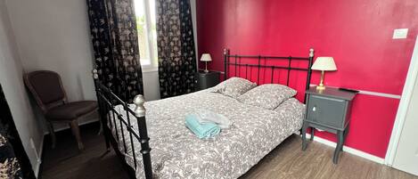 A bedroom with a bed, a chair, a nightstand, and a window with curtains.