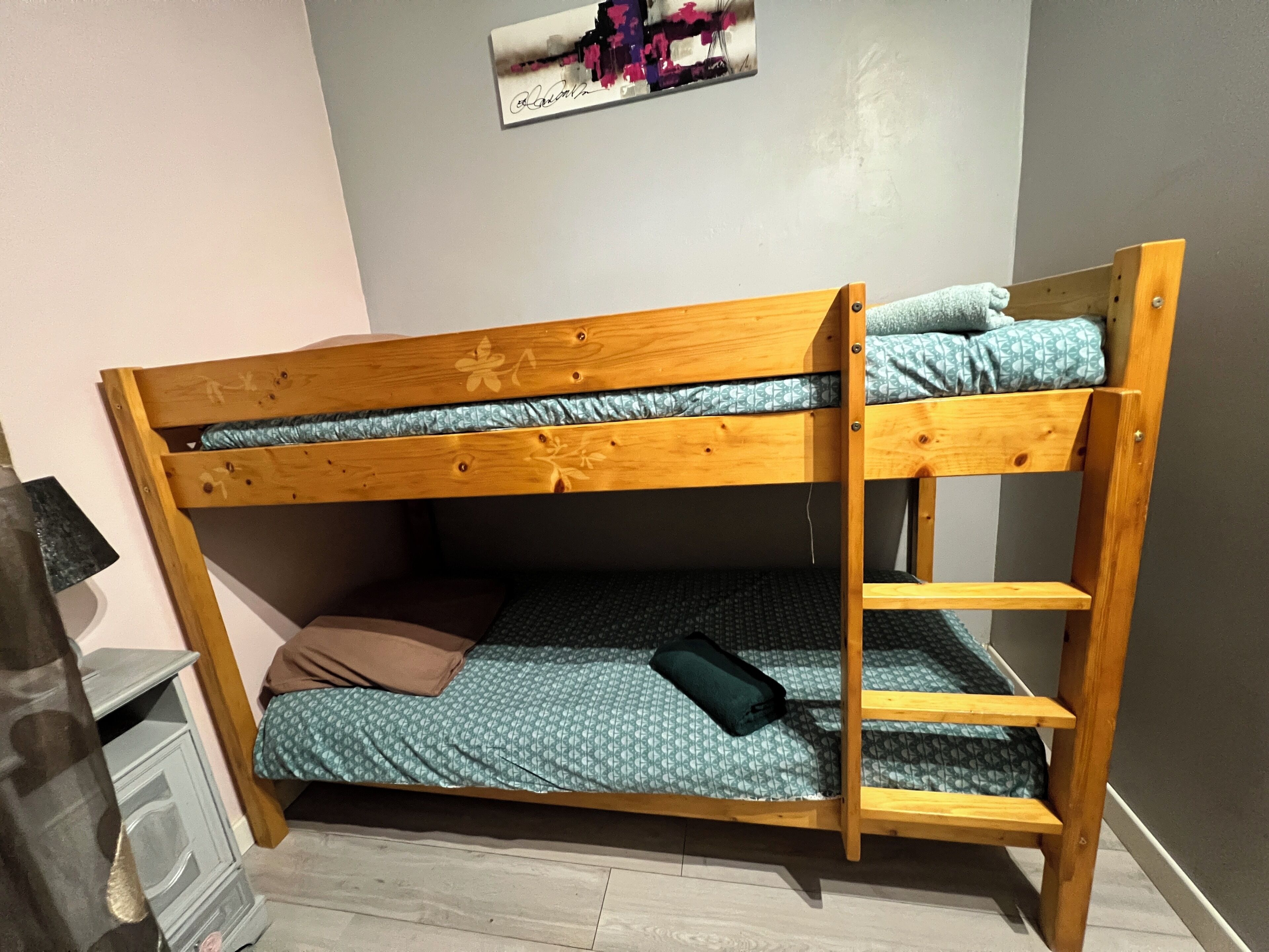 A bunk bed with a wooden frame, a lower bunk with a patterned mattress, and a top bunk with a plain mattress.