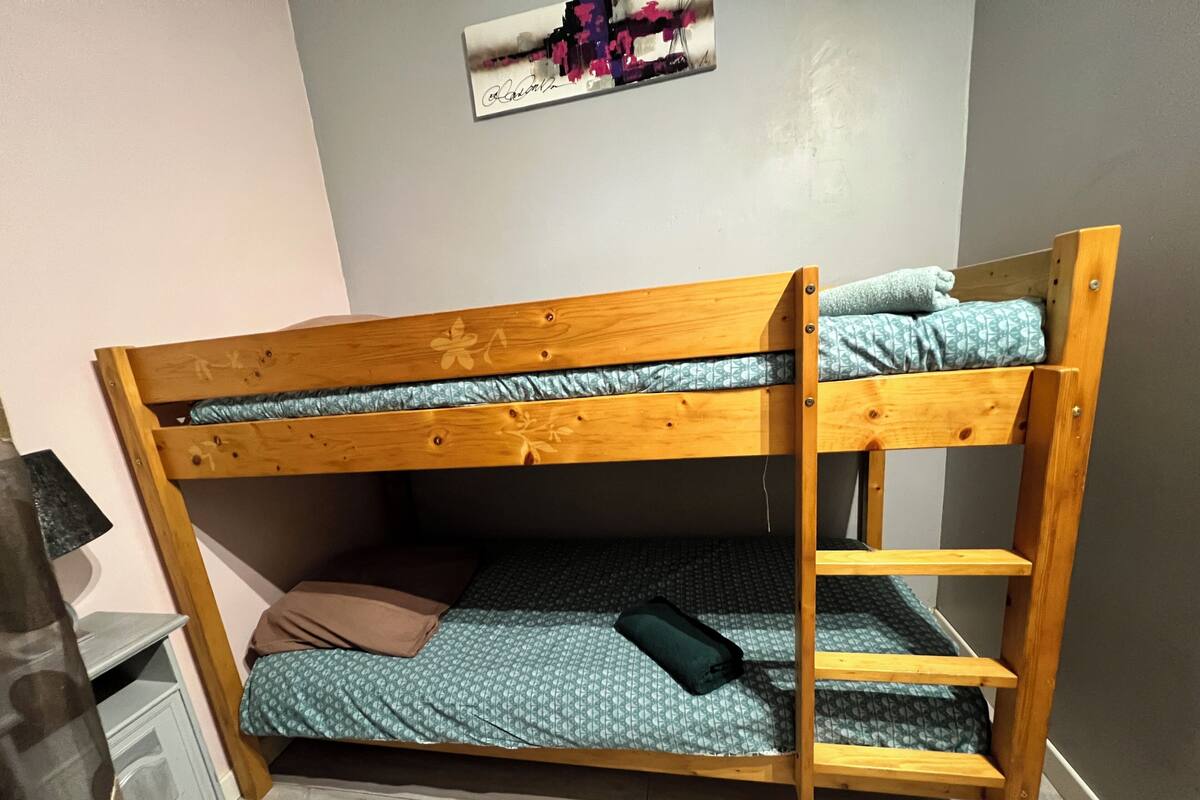 Una cama litera con estructura de madera, la litera inferior con un colchón estampado y la litera superior con un colchón liso.