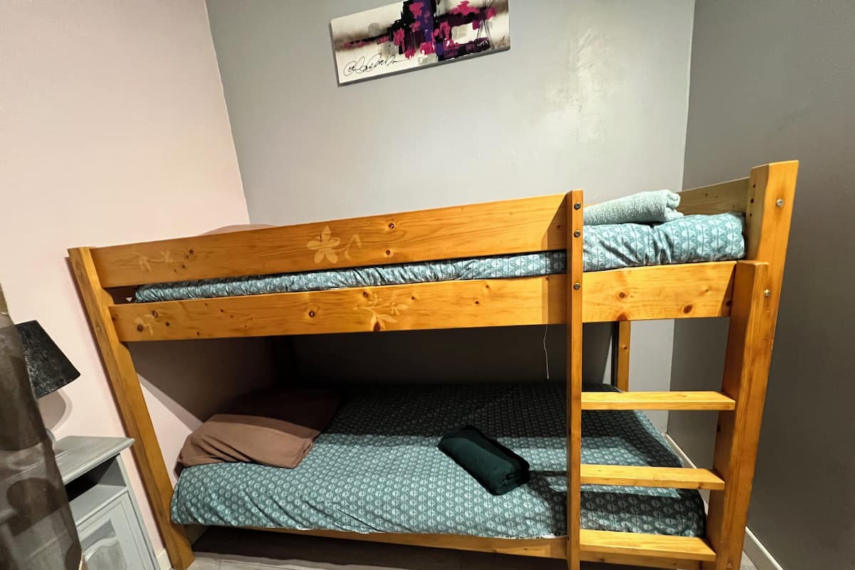 A bunk bed with a wooden frame, a lower bunk with a patterned mattress, and a top bunk with a plain mattress.