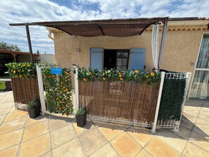 A covered outdoor area with a fence, potted plants, and a building with a window and shutters. - Domaine Les feuilles de chêne (Carpentras)