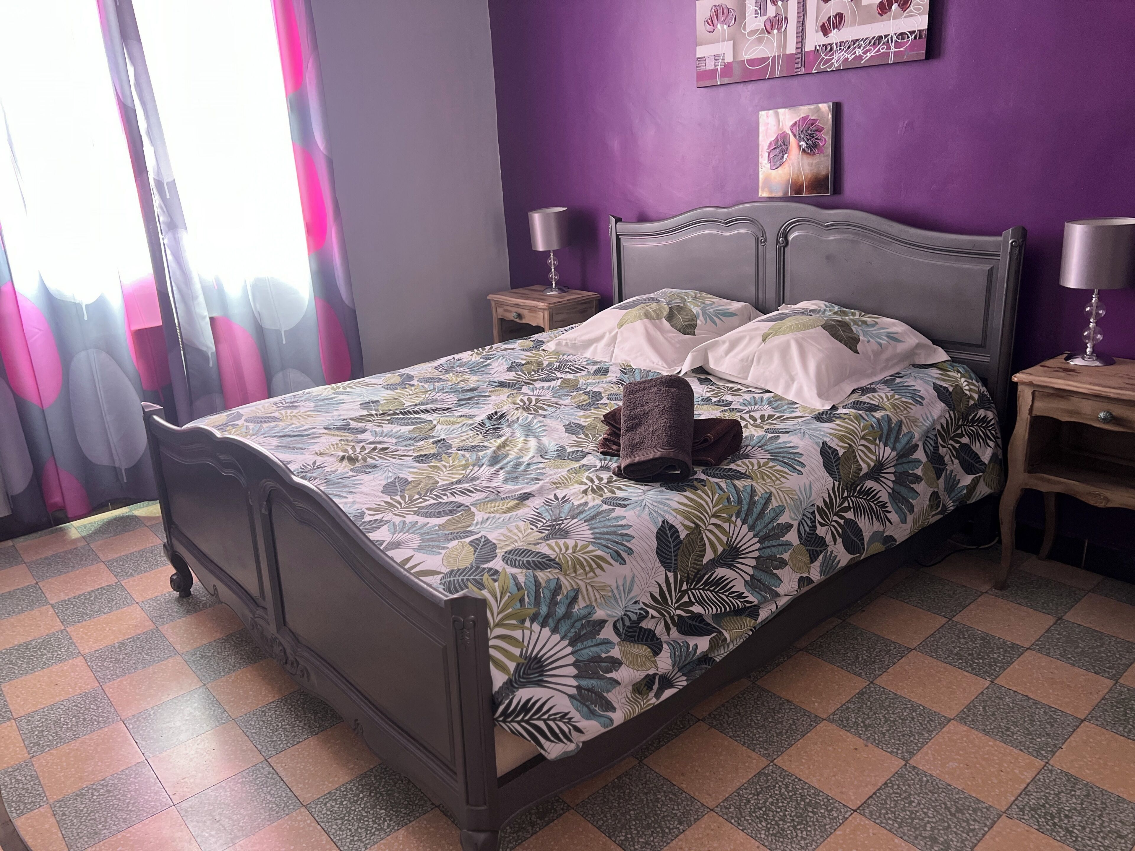 A bed with a floral bedspread, two nightstands with lamps, a window with curtains, and a wall with artwork.