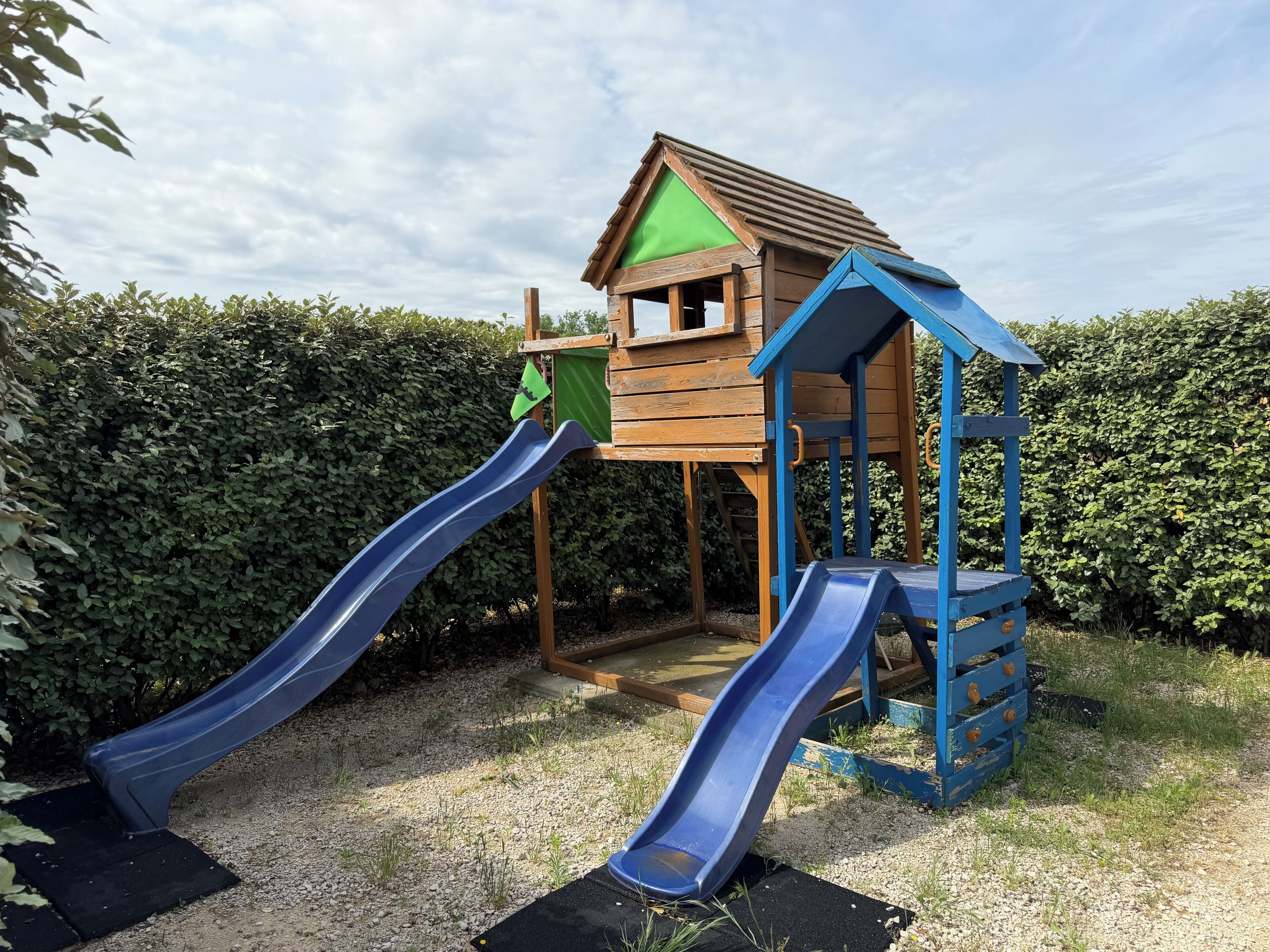 Una estructura de juego de madera con dos toboganes y una casita.
