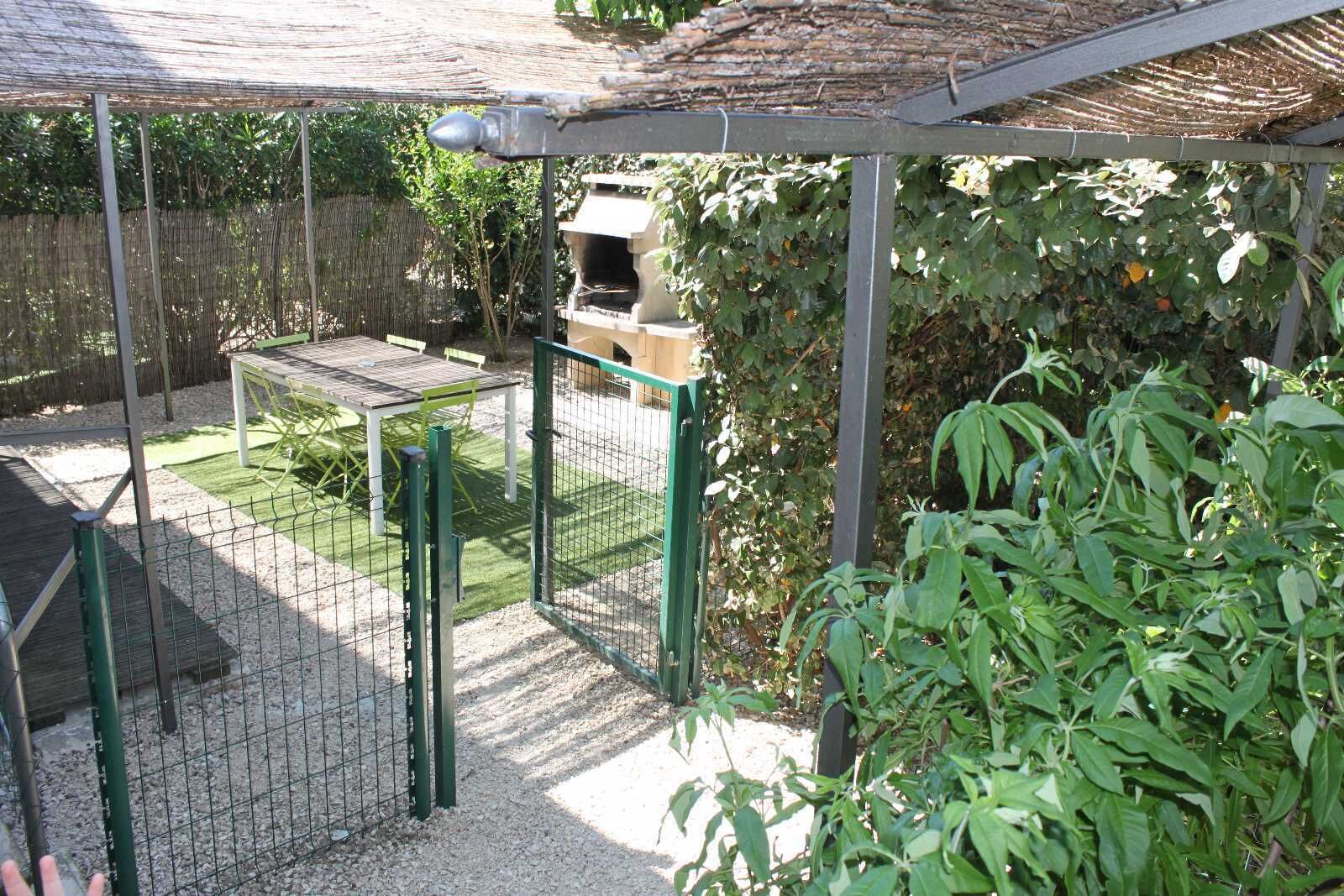 A fenced outdoor area with a table and chairs, a stone structure, and surrounding greenery.
