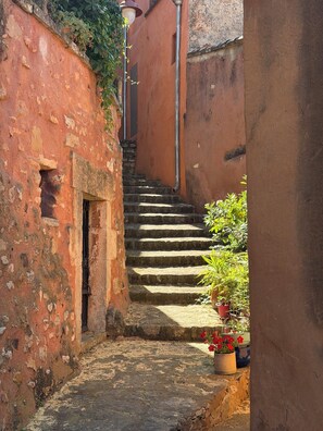 A narrow stone staircase leading up to a door, surrounded by red brick walls and potted plants. - Domaine Les feuilles de chêne (Carpentras)