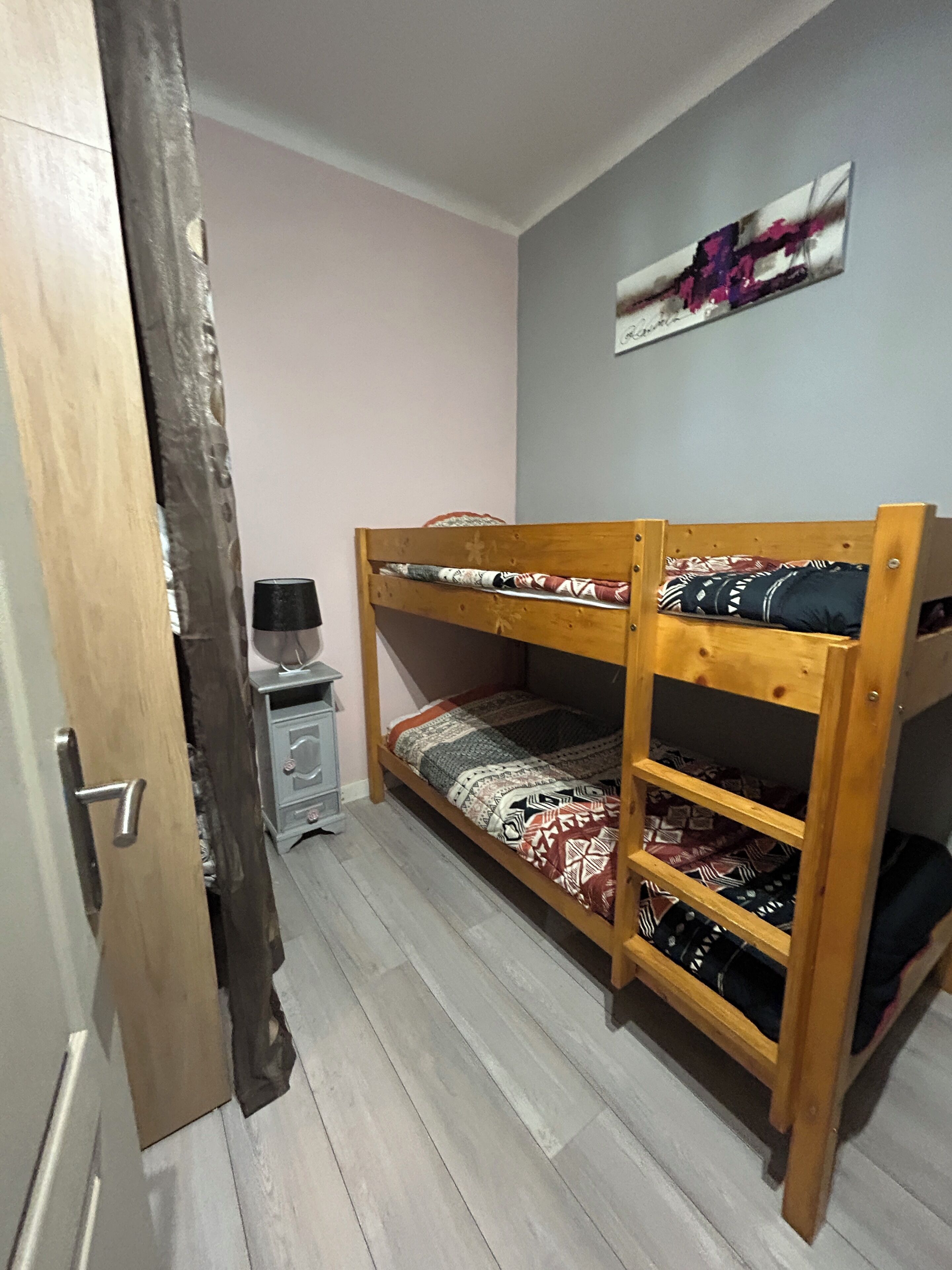 A bunk bed with patterned bedding, a small desk with a lamp, and a wall-mounted artwork.