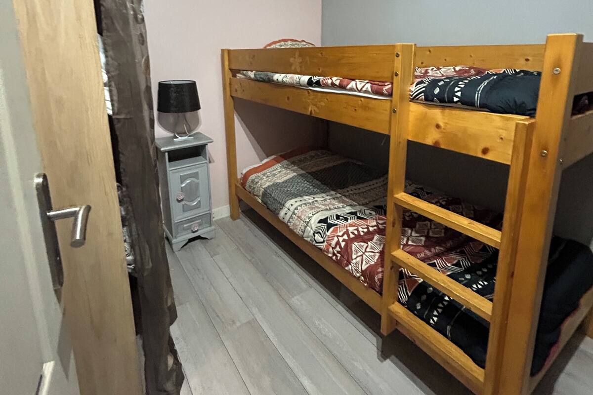 Una cama en literas con ropa de cama estampada, un escritorio pequeño con una lámpara y una obra de arte colgada en la pared.