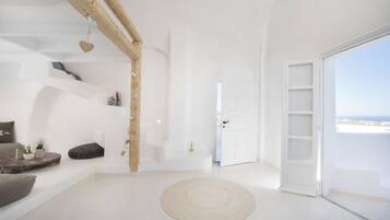 Ein heller, weißer Innenraum mit einem Holzbalken, einem runden Teppich und einer Tür, die auf einen Balkon mit Blick führt.