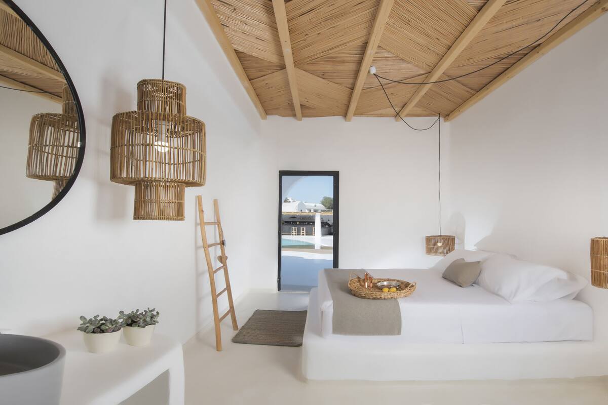 Habitación minimalista con sofá blanco, lámparas colgantes de mimbre, una escalera y vista a una piscina a través de una puerta.