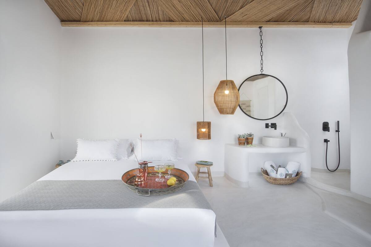 Un dormitorio moderno con cama, mesita de noche, lámpara colgante y un pequeño taburete.