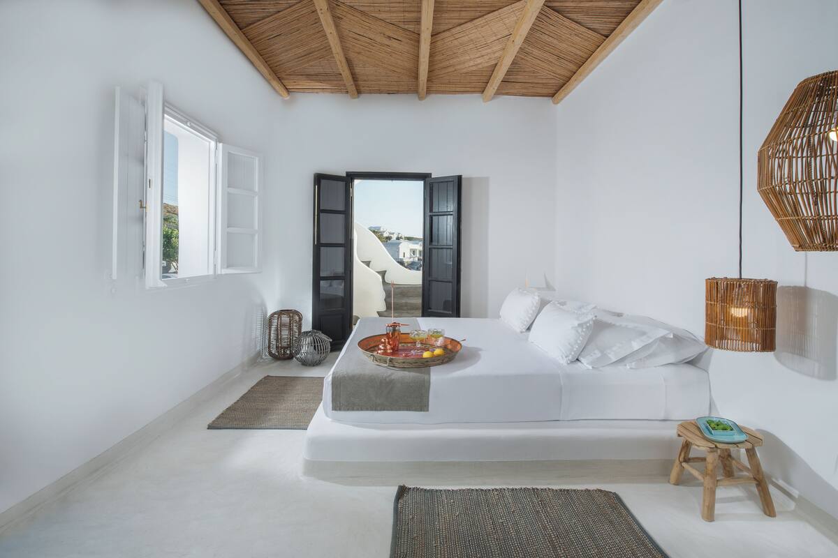 Un dormitorio minimalista con cama, mesita de noche y vistas a través de un ventanal abierto.