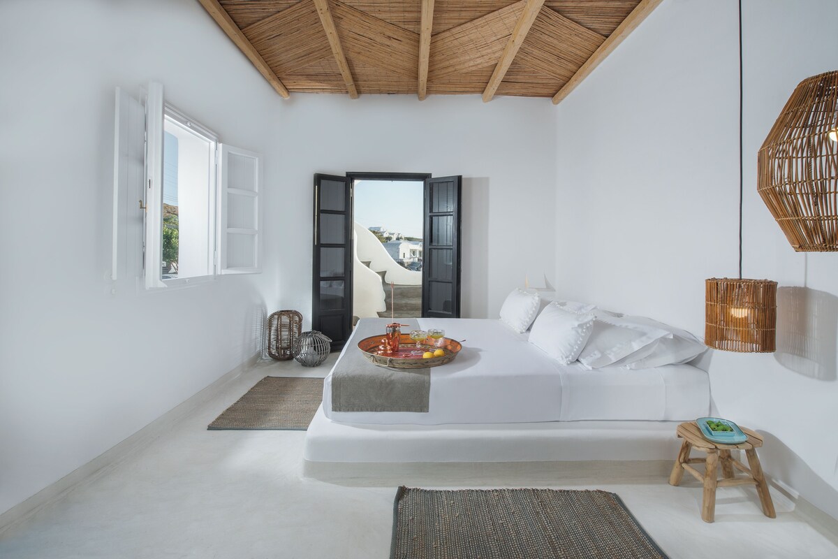 Un dormitorio minimalista con cama, mesita de noche y vistas a través de un ventanal abierto.