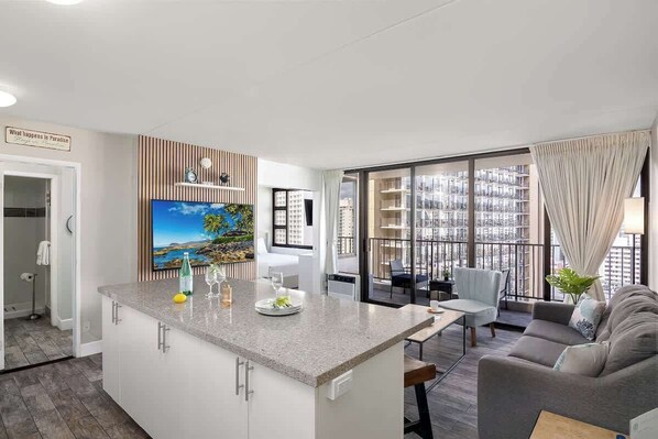 A modern living room with a kitchen island, a dining area, and large windows with a city view.