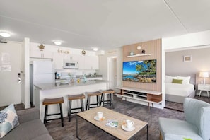 A modern hotel room with a kitchen, a dining area, a living room, and a TV.