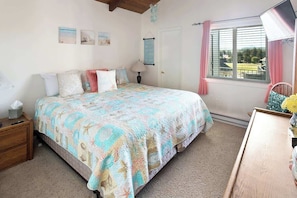 Un dormitorio con cama, mesita de noche, lámpara y una ventana con cortinas.