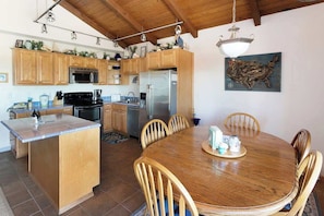 Una cocina con armarios de madera, una isla central, una mesa de comedor con sillas y una lámpara colgante.