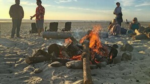 Escena de platja amb una fosa a l'entorn de roques i cadirees, gent reunida i l'oceà al fons.