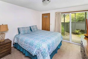Un dormitorio con cama, mesita de noche, cómoda, puerta corrediza de vidrio a un patio y ventilador de techo.