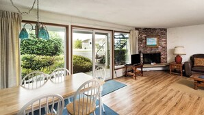 A living room with a fireplace, a dining area with chairs, and a view of the outside. - Pacific Terrace T443 (Gearhart)