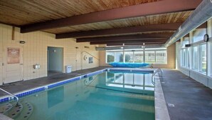 An indoor swimming pool with a wooden ceiling, a blue lifeguard chair, and a view through large windows. - Pacific Terrace T443 (Gearhart)