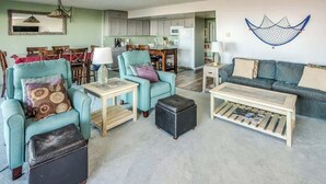 Un salon avec des fauteuils turquoise, une table basse en bois et un coin repas avec une nappe rouge.