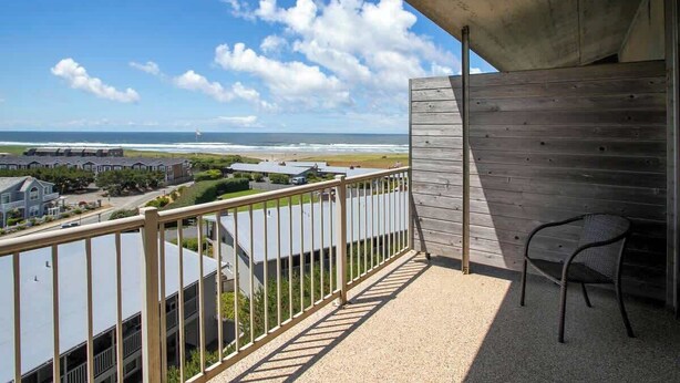 A balcony with a view of the beach and ocean, wooden railing, and a chair. - Gearhart House G700 (Gearhart)