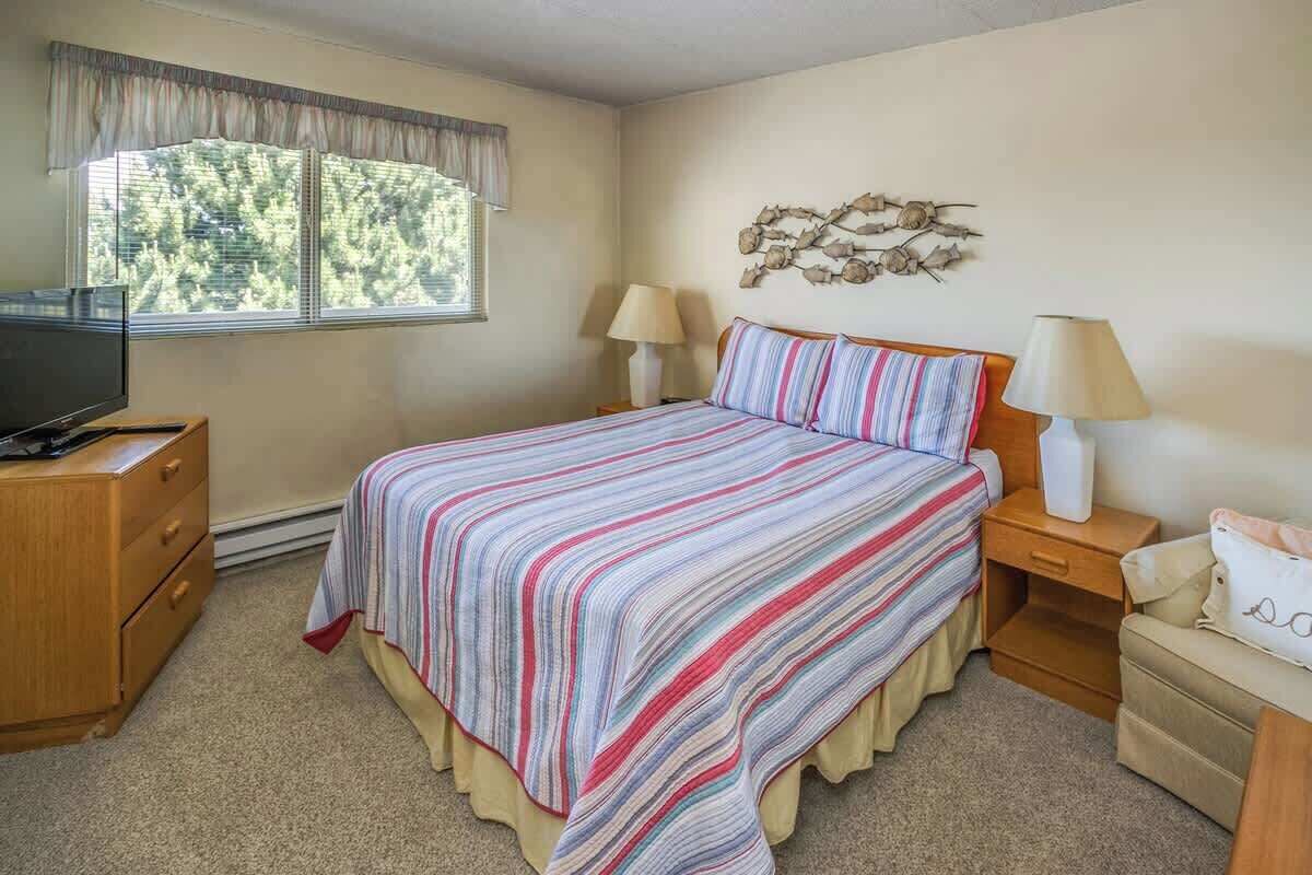 A bedroom with a bed, two bedside tables with lamps, a TV on a dresser, and a window with curtains.