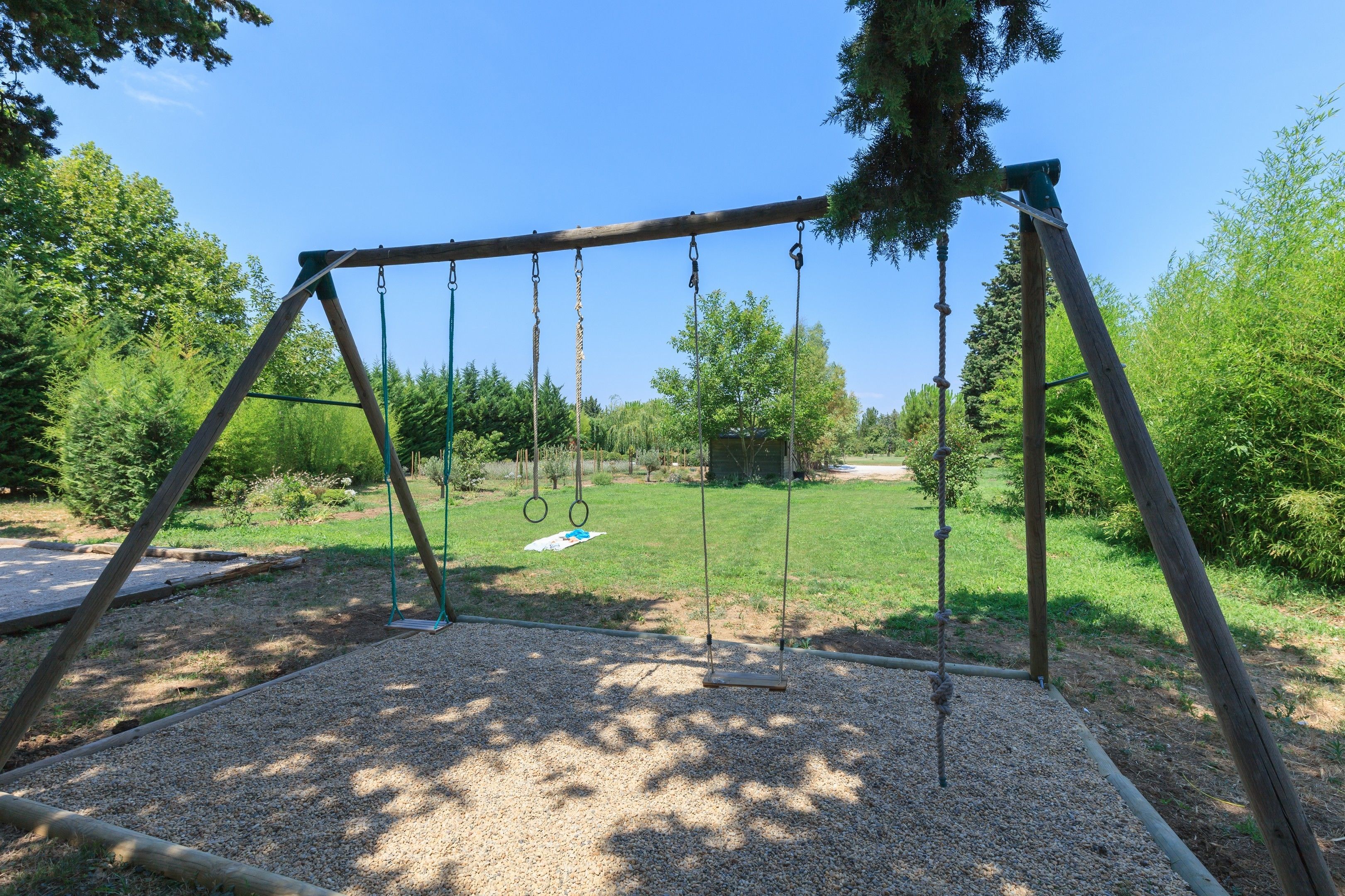 Un ensemble de balançoires en bois dans un parc, avec un sol de gravier et des arbres en arrière-plan.