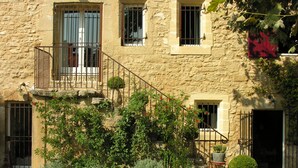 A stone building with a staircase leading to a balcony, surrounded by gravel and potted plants. - La Louvière des Bruyères (Robion)