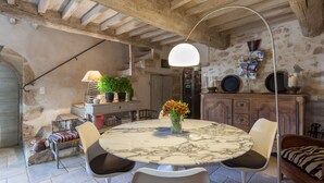 A rustic dining area with a marble table, white chairs, and a hanging light fixture. - La Louvière des Bruyères (Robion)