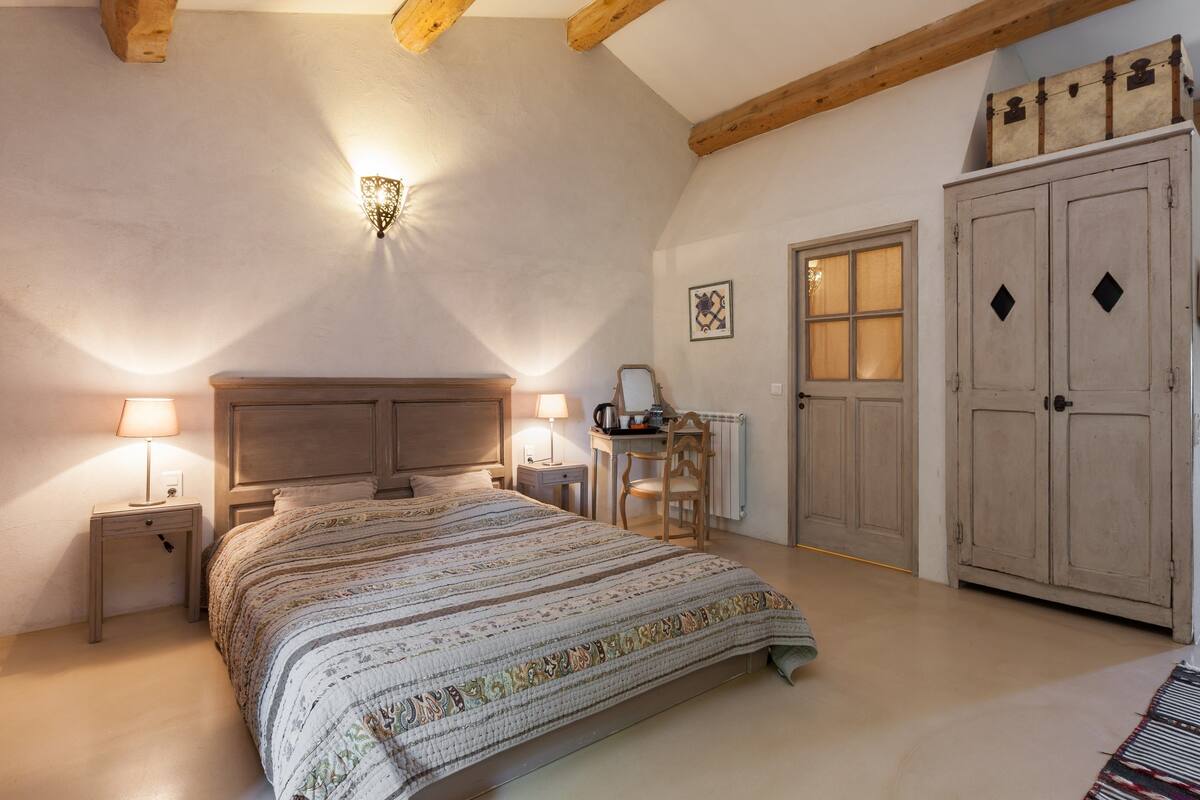 A bedroom with a large bed, bedside lamps, a desk with a chair, and a wardrobe.
