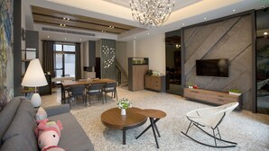 Uma sala de estar moderna com um sofá, uma mesa de centro, uma poltrona de balanço branca, um espaço de refeições com mesa e cadeiras, um espaço de cozinha com uma TV e um candelabro.