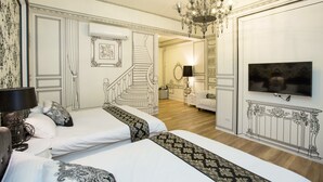 Quarto de hotel com duas camas, um candelabro, uma TV e uma escada que leva a outro espaço.
