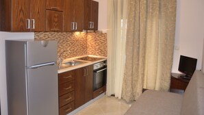 A compact kitchen with wooden cabinets, a stainless steel refrigerator, a built-in oven, and a sink. - 4-You Residence (Sithonia)