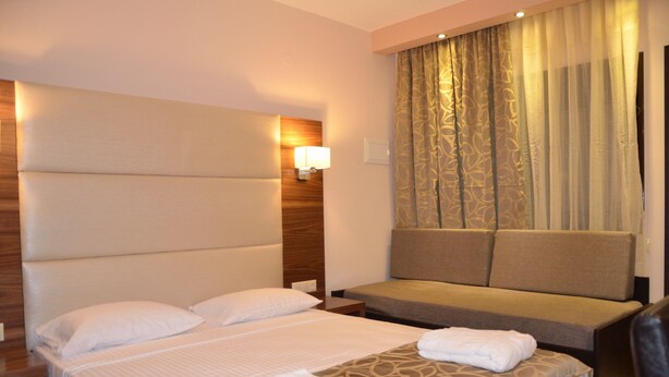 A hotel room with a large bed, a sofa, a nightstand, and a wall-mounted lamp. - 4-You Residence (Sithonia)