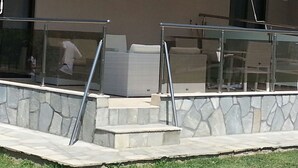 A building with a stone retaining wall, a glass railing, and outdoor seating. - 4-You Residence (Sithonia)