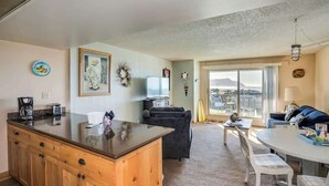 A living room with a sofa, a dining table with chairs, a kitchen area with a wooden cabinet, and a large window with a view. - Gearhart House G670 (Gearhart)