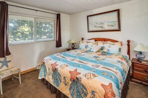 A bedroom with a bed, a nightstand, a lamp, a window with curtains, a picture on the wall, and a small table with a star decoration.